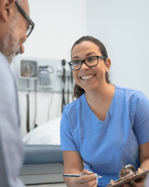 Nurse leans forward, smiling while talking to a patient.