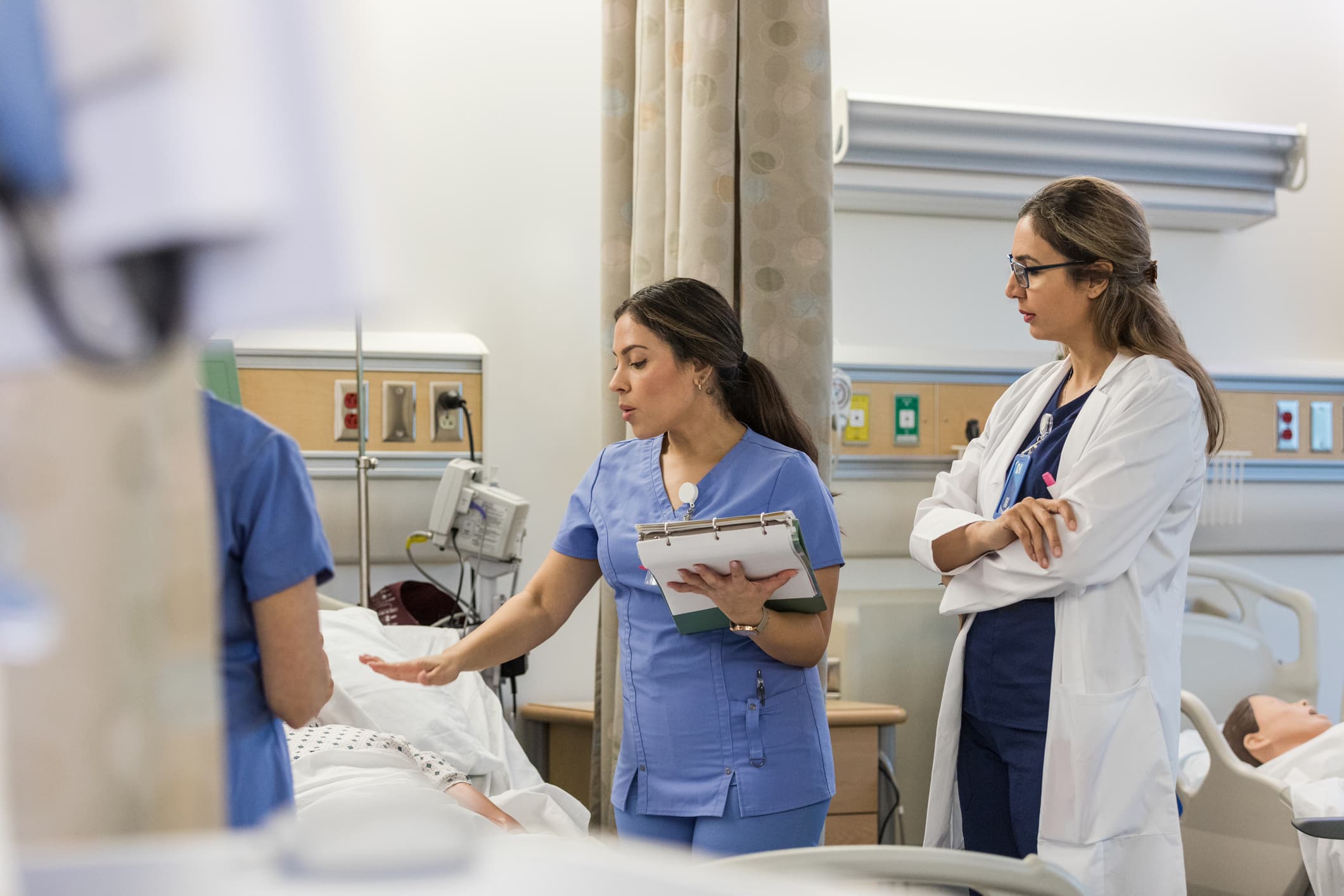 A trainer is observing a nurse at a patient's bedside.